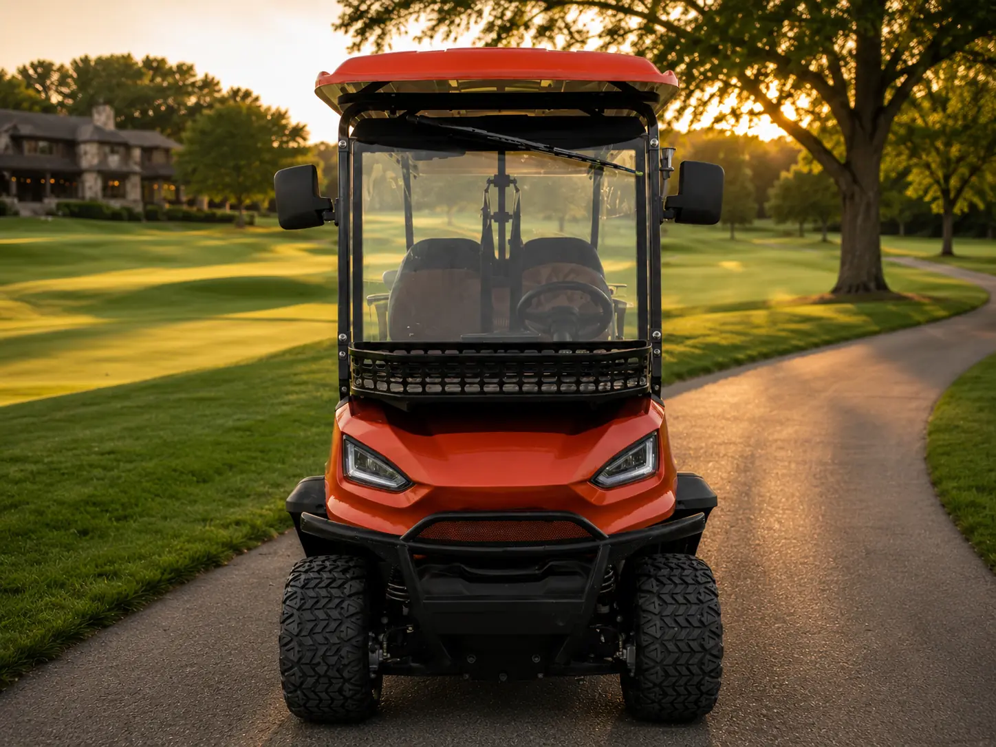 Front view of an orange Oreion electric golf cart on a luxury golf course